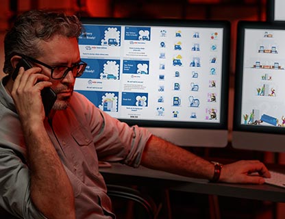 Photo of a man at desk talking on mobile phone with computers in background