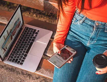 Photo looking down at a woman's lap while she holds mobile phone and laptop next to her